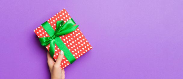 Плоский узор женщины, держащей в руках подарочную упаковку и украшенную бантом на фиолетовом фоне с копировальным пространством. Концепция Рождества и праздника. - Фото, изображение