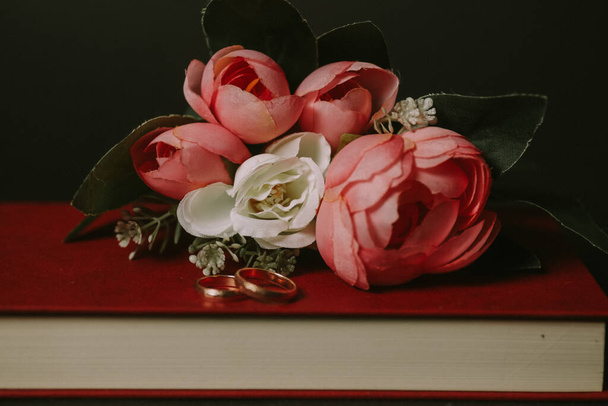 wedding rings on red book and artificial peony bouquet - Photo, image