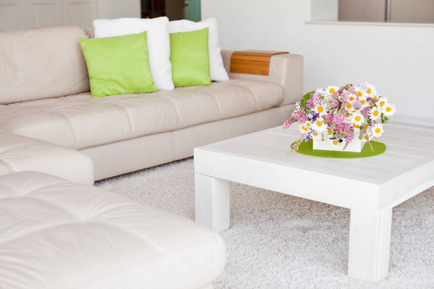 Interieur mit Blumen, Wohnkomfort, einem Tisch mit Blumen und einem gemütlichen Sofa daneben. - Foto, Bild