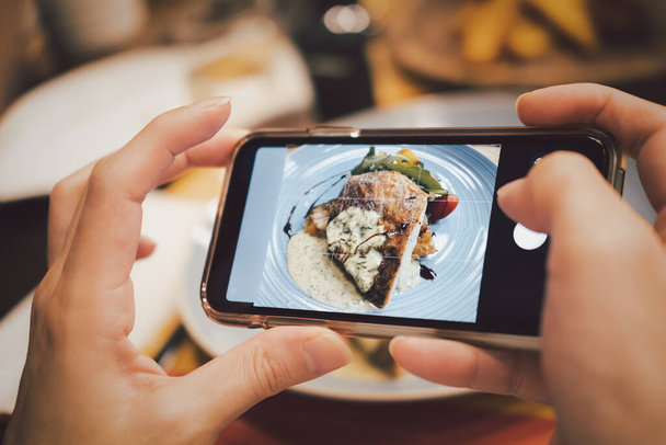 Take a photo by smart phone of sea bass fillet steak with lemon sauce served with vegetable on plate - Fotografie, Obrázek