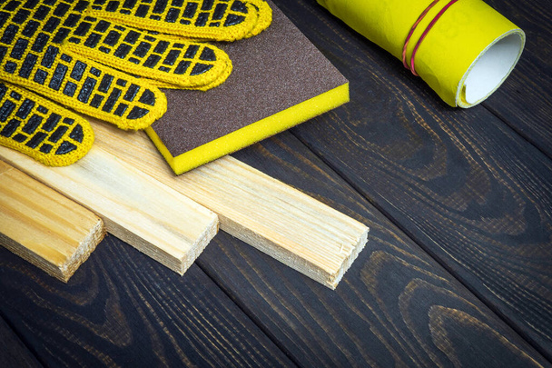 Werkhandschoenen en geel schuurpapier voor het schuren van houten platen. Het idee van een werkomgeving voor het werk van meesterbouwers - Foto, afbeelding