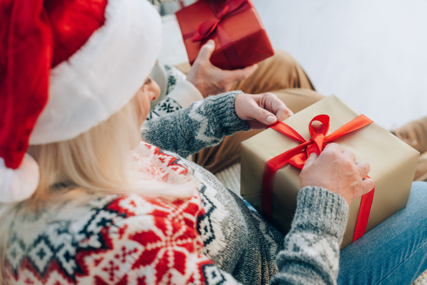 Selektiver Fokus der Seniorin im Weihnachtsmannhut beim Öffnen der Geschenkbox in der Nähe ihres Ehemannes - Foto, Bild