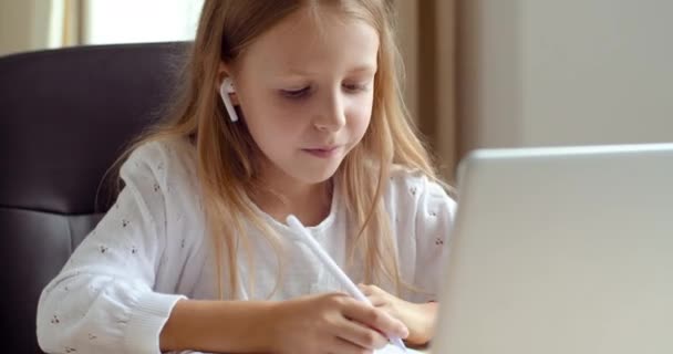 Távoktatási koncepció. Aktív iskoláslány tanul online laptoppal jegyzetel a másolókönyvben. Fülhallgatós tini hölgy, webkamerába néz, integet, üdvözöl, otthon ül. - Felvétel, videó