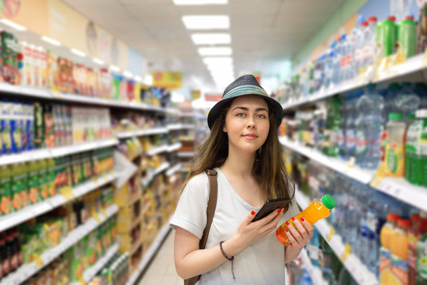 Jonge mooie vrouw kiest een fles sap in de supermarkt en controleert de QR-code op het etiket. Het concept van moderne technologie en winkelen in de winkel. - Foto, afbeelding