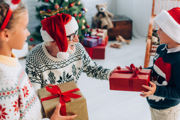 サンタ・ハットの高齢者の選択的焦点は孫からクリスマスプレゼントを取り - 写真・画像