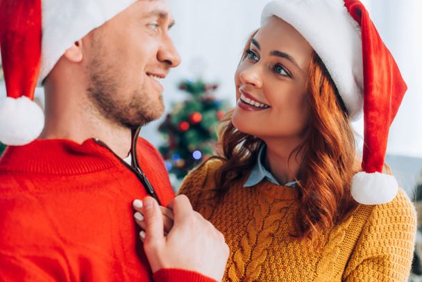 selective focus of happy woman in santa hat touching smiling husband - Fotografie, Obrázek