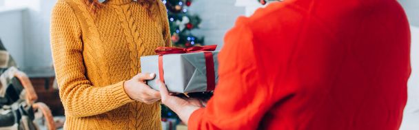 selective focus of man presenting christmas gift to wife, panoramic shot - Фото, изображение