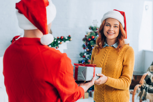 back view of man in santa hat presenting christmas gift to happy wife  - Photo, Image