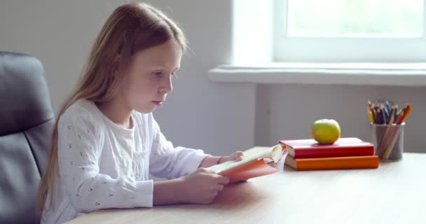 Χαριτωμένη εστιασμένη μαθήτρια μικρό παιδί κάθεται στο τραπέζι στο σπίτι στο σχολείο στην τάξη, διαβάζει το βιβλίο δυνατά, κάνει την εργασία, προετοιμάζεται για εξετάσεις δοκιμή, μαθαίνει από τον εαυτό της κατά τη διάρκεια καραντίνας του ιού πανδημία - Πλάνα, βίντεο