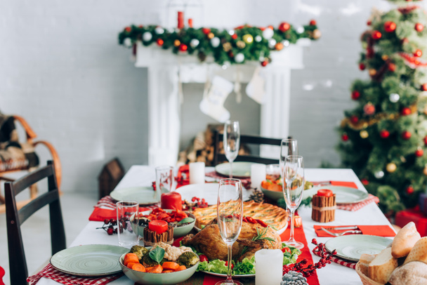селективный акцент стола подается с праздничным ужином, елкой и камином на фоне украшенной елочной ветви - Фото, изображение
