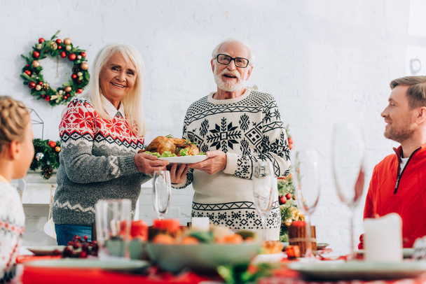 Selective focus of elderly people with turkey near family and festive table - Foto, Imagen
