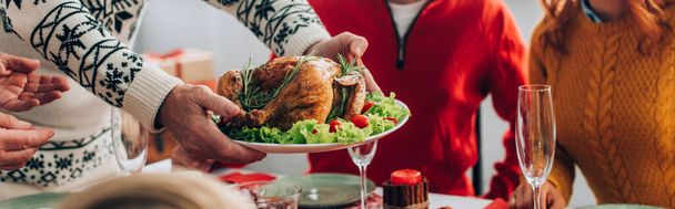 Panoramic shot of man serving turkey on festive table near family at home - Foto, afbeelding