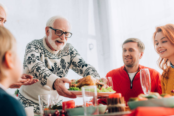 Selective focus of happy grandfather serving turkey on festive table near family - Фото, изображение