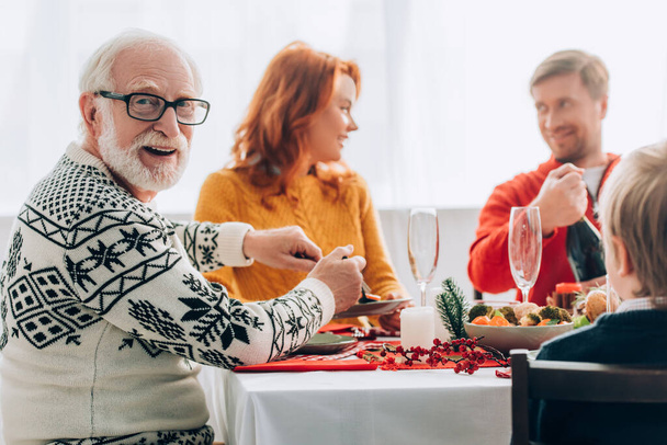 Selective focus of grandfather serving food near couple talking, at home - Foto, afbeelding