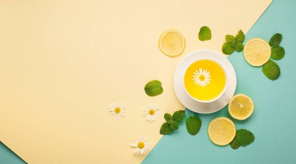 Chá de ervas de flor de camomila, limão e gengibre com mel no fundo de papel amarelo e azul colorido combinado. Chá medicinal picante para estação de outono ou inverno. - Foto, Imagem