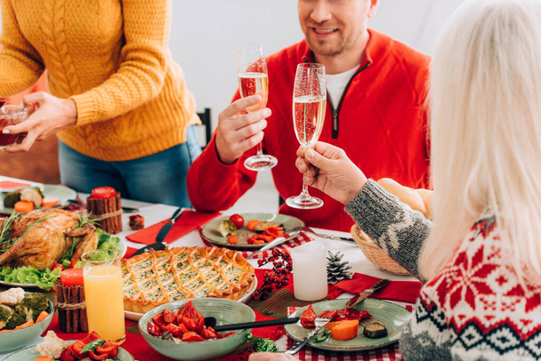Vista cortada de mulher e homem segurando copos com champanhe, sentado perto da família à mesa - Foto, Imagem