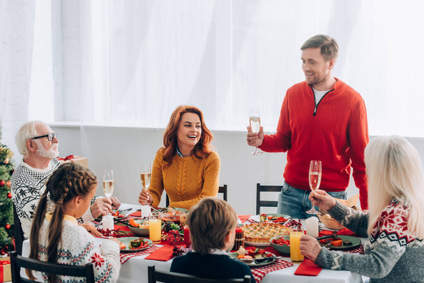 Smiling man with champagne glass saying speech near family at festive table at home - Photo, Image