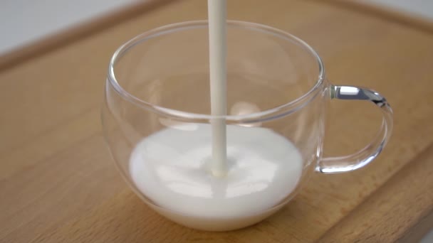 Il kefir spesso bianco o lo yogurt è versato in una tazza di vetro con una maniglia su un tagliere di legno primo piano. Rallentatore - Filmati, video