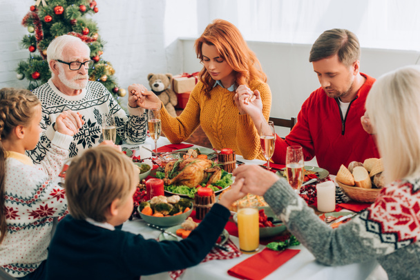 Family holding hands while sitting at festive table with thanksgiving dinner - Фото, зображення