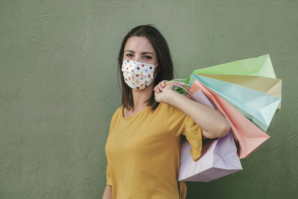 Junge glückliche Frau mit medizinischer Maske hält eine Einkaufstasche über grünem Hintergrund - Foto, Bild