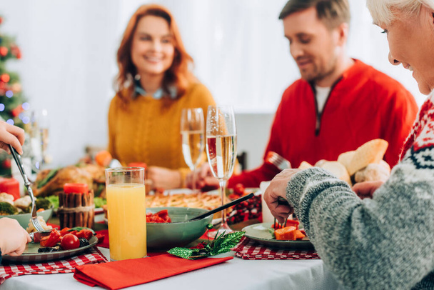 Selective focus of smiling grandma eating, sitting at festive table with family - 写真・画像