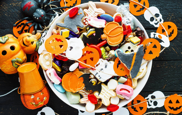Halloween Jack o Lantern candy bowl with candy and halloween cookies Trick or Treat on black wooden background - 写真・画像