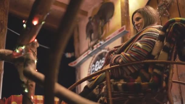 zbliżenie ciężarnej kobiety uśmiecha się i huśta na krześle przed przytulnym domu w Boże Narodzenie - Materiał filmowy, wideo