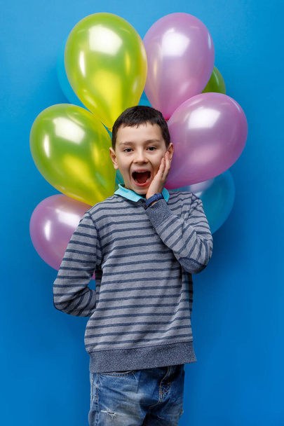 Emotional smile little boy holding  ballons on blue background. Little child is going to throw somebody his ballon. - Fotoğraf, Görsel