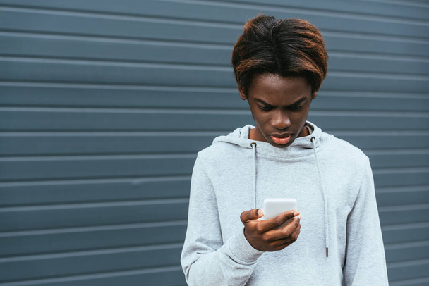 Afectado adolescente afroamericano utilizando el teléfono inteligente al aire libre  - Foto, Imagen