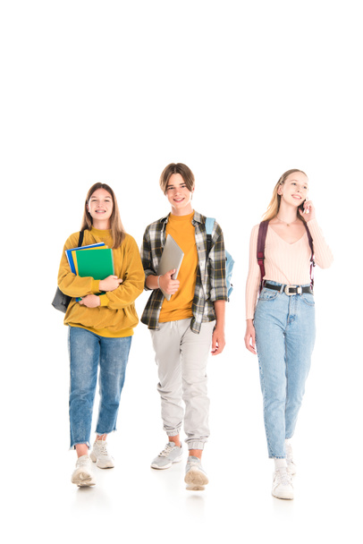 Lachende tieners met rugzakken, notitieboekjes en smartphone lopen op witte achtergrond - Foto, afbeelding