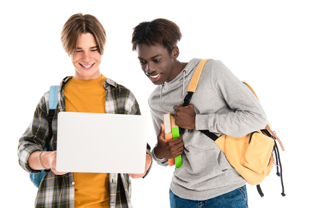 African american teenager with backpack and books looking at laptop near friend isolated on white - Foto, immagini