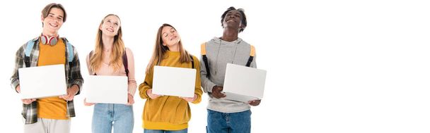 Panoramic crop of positive multicultural teenagers holding laptops isolated on white - Фото, изображение
