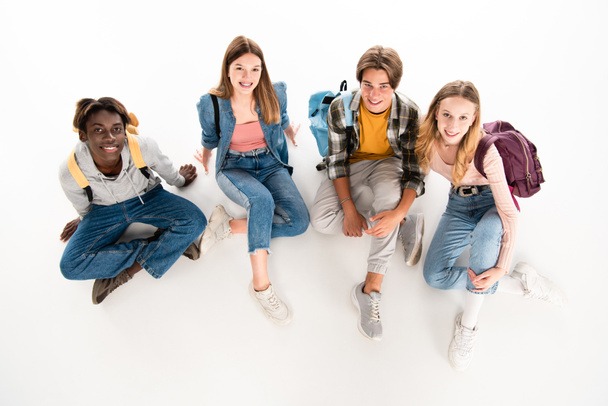 Overhead view of multiethnic teenagers with backpacks smiling at camera on white background - Foto, immagini