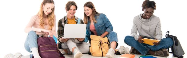 Cabeçalho do site de adolescentes multiétnicos sorridentes olhando para laptop perto de livros e mochilas em fundo branco - Foto, Imagem
