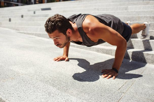 Young man exercising outside. Hardworking athlete doing push up exercise alone at steps outside. Man training and working on his body shape. Getting better. - Фото, зображення