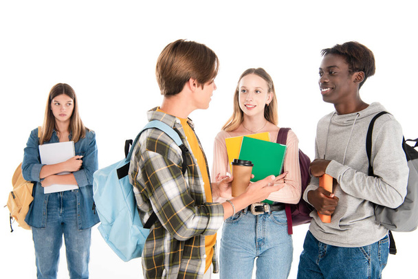 Sonrientes adolescentes multiétnicos con mochilas hablando cerca chica triste aislado en blanco - Foto, imagen