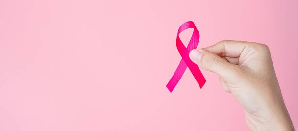 October Breast Cancer Awareness month, adult Woman hand holding Pink Ribbon on pink background for supporting people living and illness. International Women, Mother and World cancer day concept - Fotoğraf, Görsel