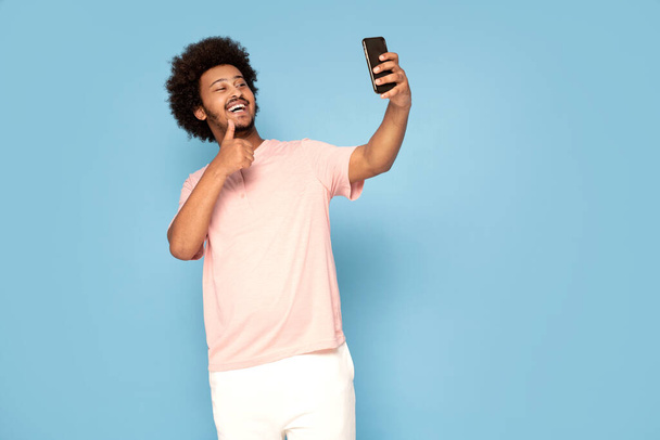 Cheerful young african guy in casual t-shirt holding mobile phone , smiling. - Foto, immagini