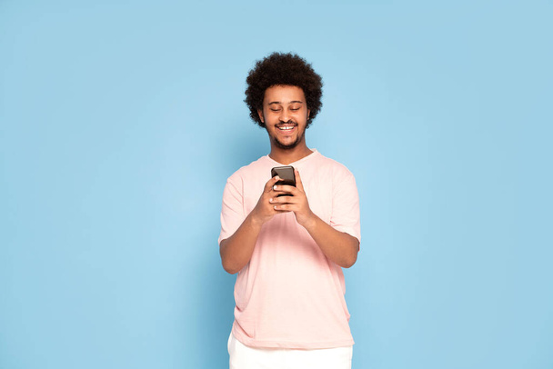 Cheerful young african guy in casual t-shirt holding mobile phone , smiling. - Foto, Bild