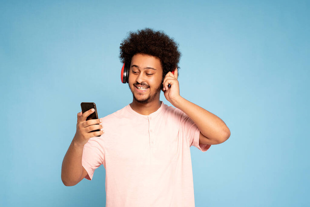Cheerful young african guy in casual t-shirt holding mobile phone , smiling. - Photo, Image