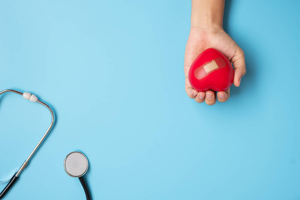 Doktor eli kırmızı kalp şeklinde ve steteskop mavi arka planda. Sağlık, Hayat Sigortası ve Dünya Kalp Günü konsepti - Fotoğraf, Görsel