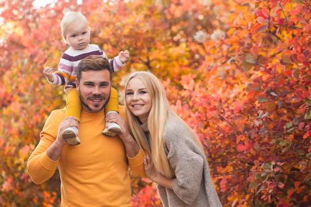 A married couple and their little daughter are walking in the autumn forest. People are wearing white pants and brightly colored sweaters. Healthy lifestyle. Family values - 写真・画像