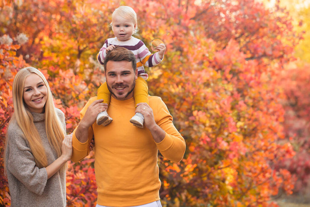 A married couple and their little daughter are walking in the autumn forest. People are wearing white pants and brightly colored sweaters. Healthy lifestyle. Family values - Фото, зображення