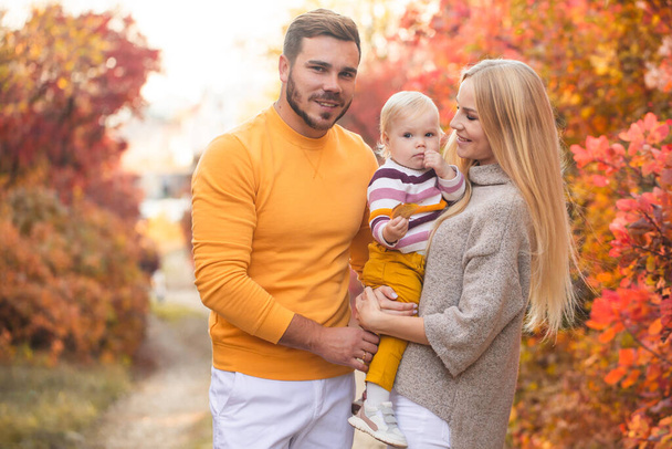 A married couple and their little daughter are walking in the autumn forest. People are wearing white pants and brightly colored sweaters. Healthy lifestyle. Family values - Foto, imagen