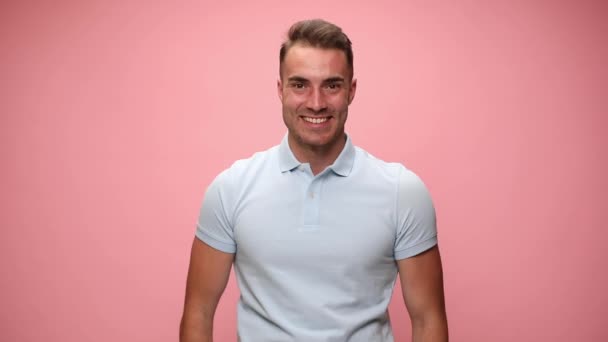 attractive casual man is very excited, making a thumbs up gesture with both hands and celebrating succes on pink background - Кадры, видео