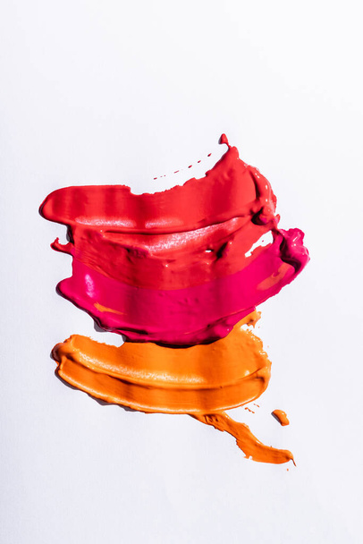 top view of red, orange and pink abstract brushstrokes on white background - 写真・画像