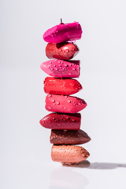 stack of wet colorful lipsticks on white background - Фото, изображение