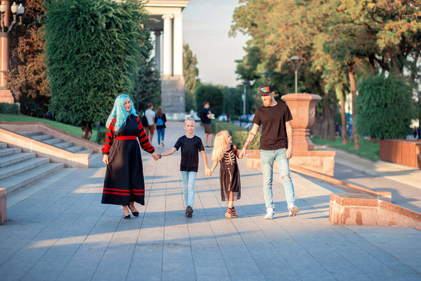 Ασυνήθιστη οικογένεια τεσσάρων ατόμων περπατούν χέρι-χέρι στο πάρκο. Σύγχρονη τάση, ασυνήθιστο μαύρο στυλ πανκ - Φωτογραφία, εικόνα