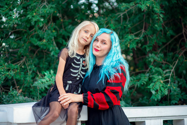 Młoda kobieta z niebieskimi włosami przytulająca się do swojej blond córki w sukience z wzorzystym szkieletem - Zdjęcie, obraz