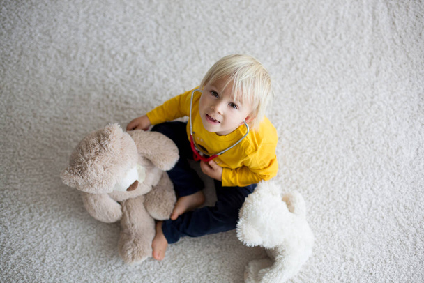 Sweet toddler child, playing doctor, examining teddy bear toy at home, isolated background - Photo, Image